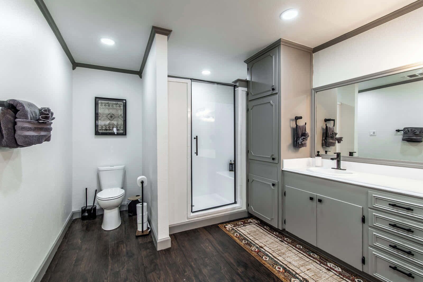 A modern bathroom with a glass shower, white toilet, and grey cabinets.