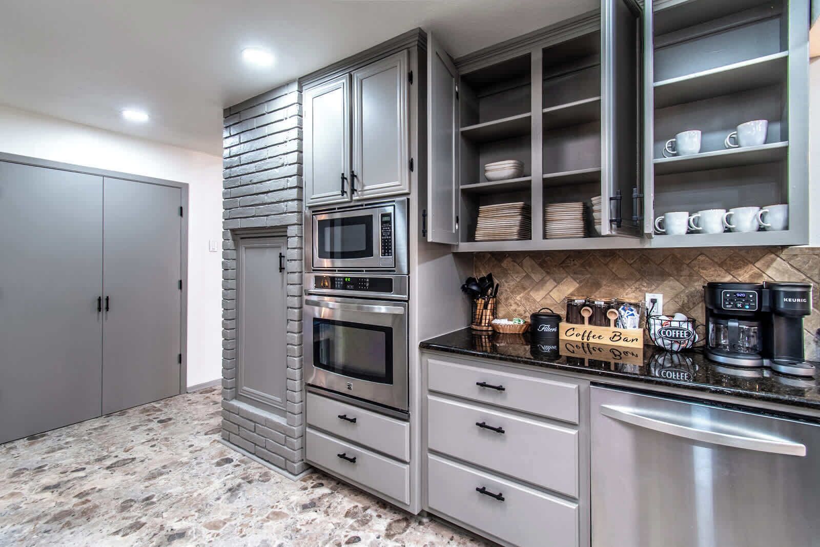 A kitchen with grey cabinets, a microwave, a coffee station, and a coffee maker.