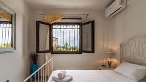 Un dormitori amb un llit, una finestra amb cortines, un aparell d'aire condicionat i una taula de nit amb una làmpada.