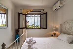 Ein Schlafzimmer mit Bett, einem Fenster mit Vorhängen, einer Klimaanlage und einem Nachttisch mit Lampe.
