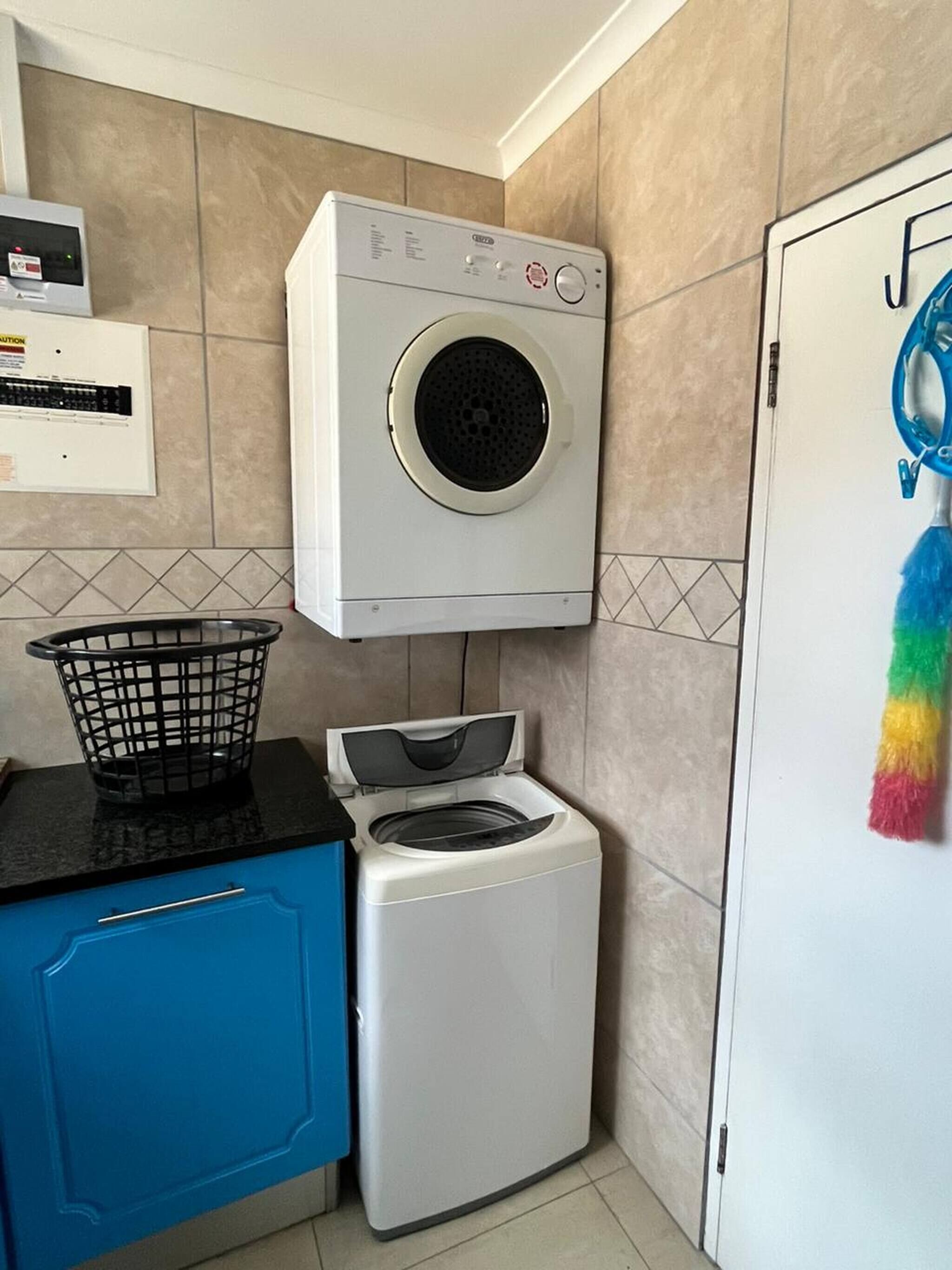 A compact laundry area with a washing machine and dryer, a blue cabinet, and a wall-mounted control panel.