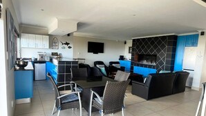 Une cuisine moderne avec des meubles bleus, un coin repas avec des chaises en osier et une cheminée intégrée.