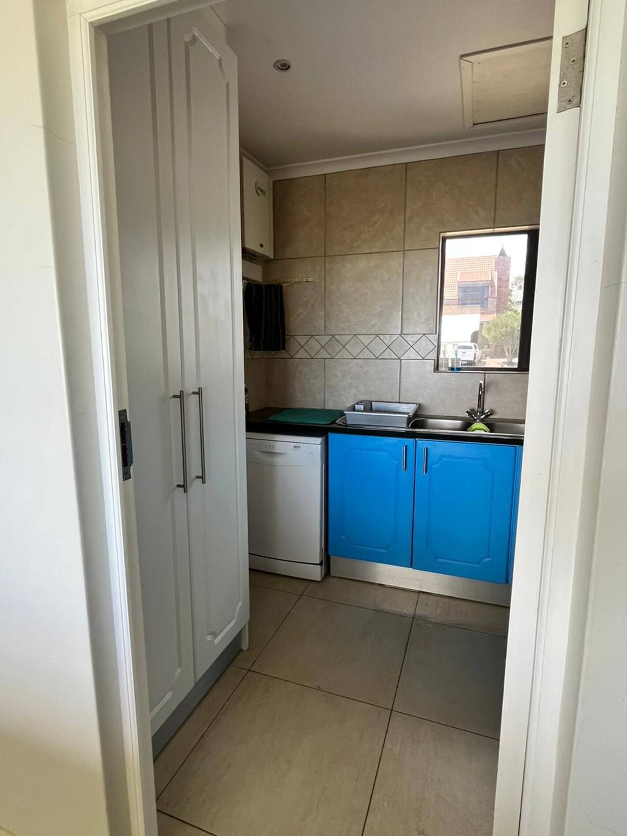 A compact kitchen with a dishwasher, blue cabinets, and a window.