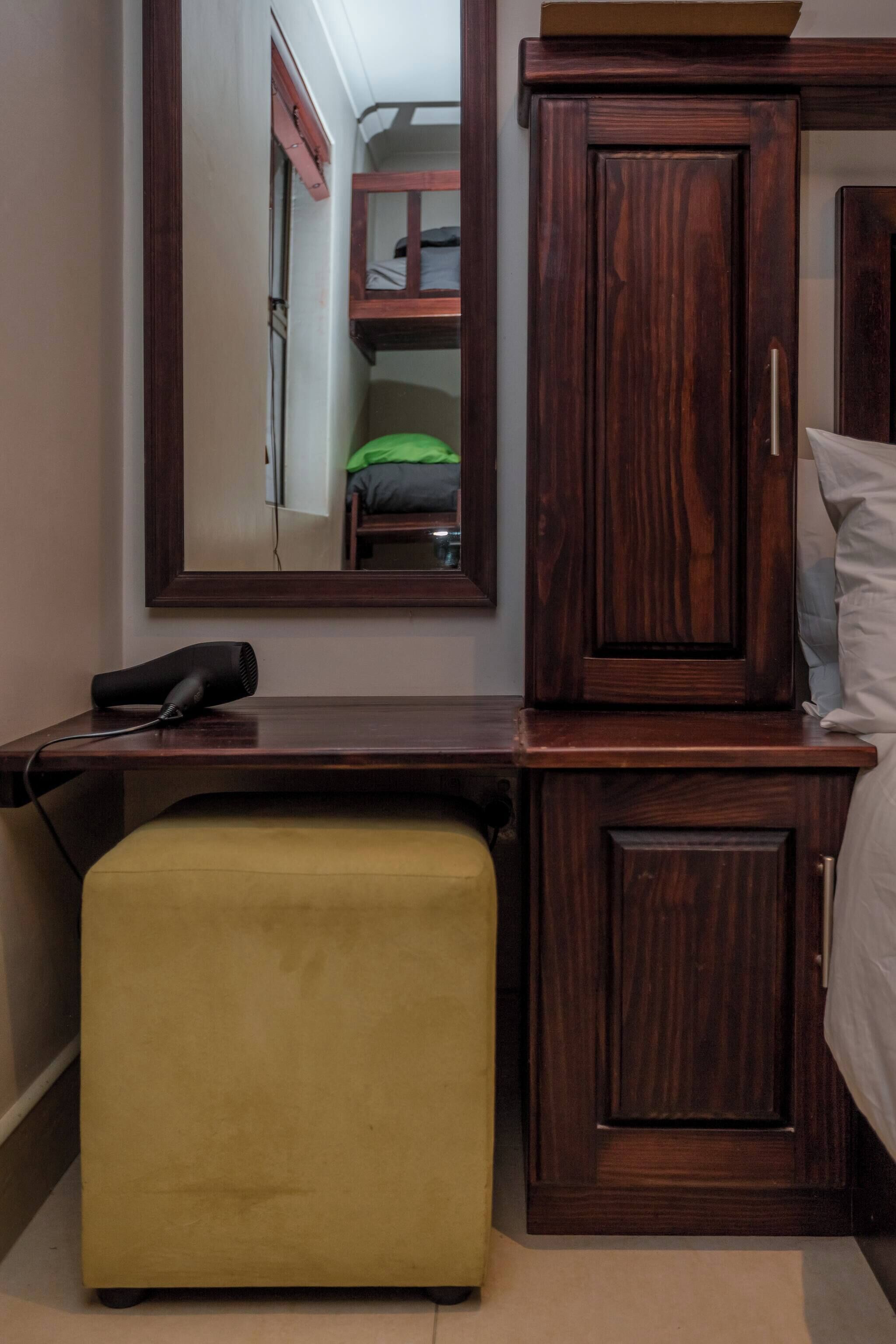 Un dormitorio con un armario de madera, una mesita de noche, un espejo y una cama litera al fondo.