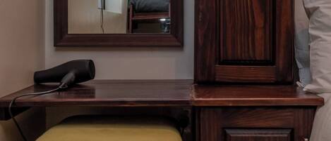 Un dormitorio con un armario de madera, una mesita de noche, un espejo y una cama litera al fondo.