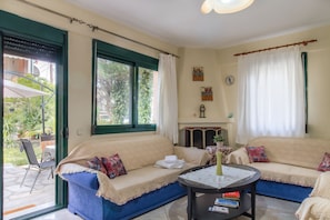 Ein gemütliches Wohnzimmer mit einer Sofagarnitur, einem kleinen runden Tisch und Blick ins Freie durch ein großes Fenster.
