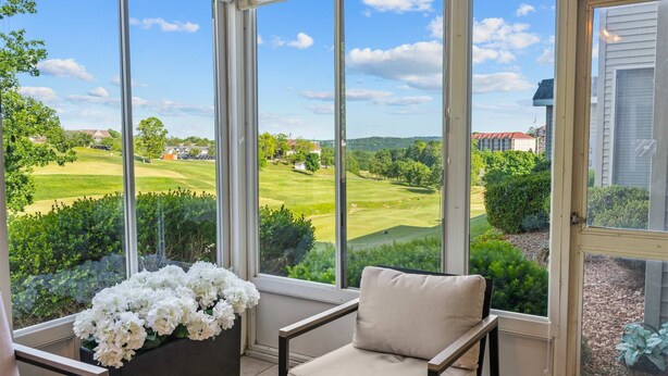 Un invernadero con vistas a un campo de golf, una silla y un arreglo floral.