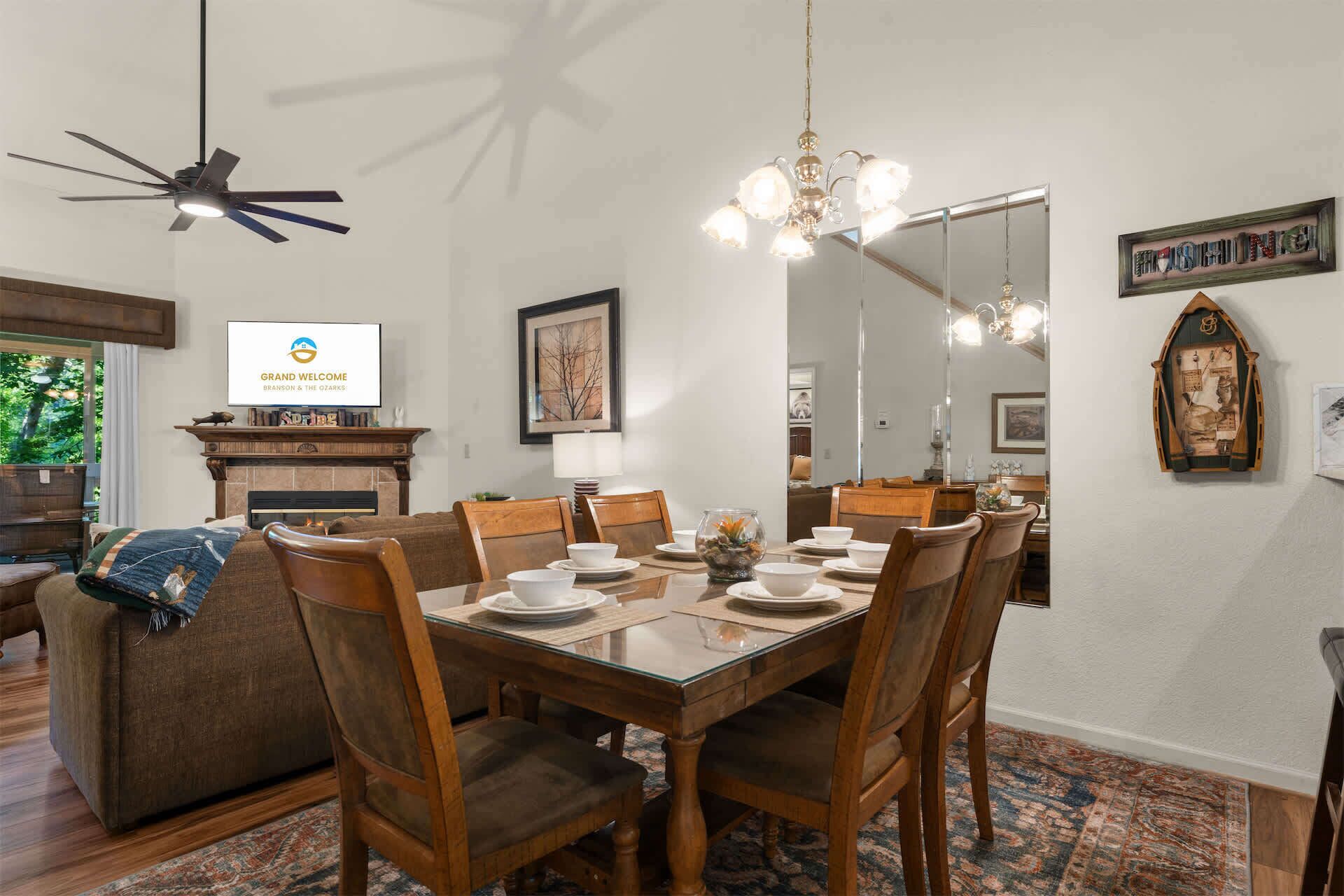 Comedor con mesa de madera dispuesta para seis personas, rodeada de sillas, una araña y una chimenea.