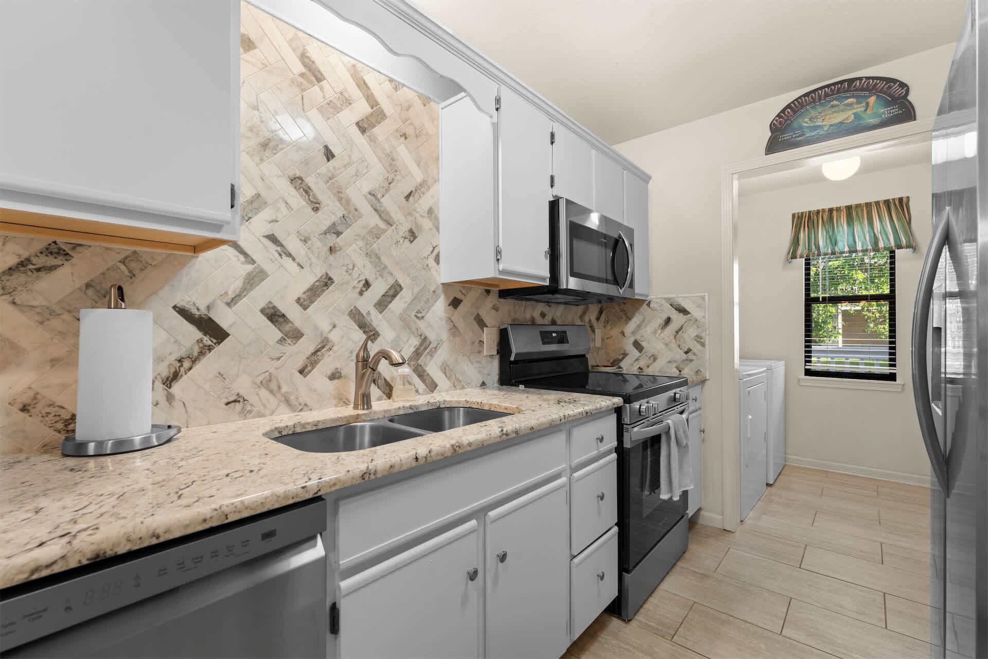 A kitchen with a herringbone tile backsplash, stainless steel appliances, and a window with a view of greenery.