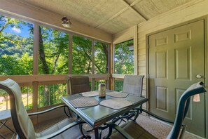 Eine überdachte Veranda mit Tisch und Stühlen, großen Fenstern und einer Tür.