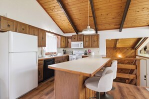 Eine Küche mit Holzausstattung, einem weißen Kühlschrank, einer Mikrowelle, einem Spülbecken und einer Holzeile mit Barhocker.