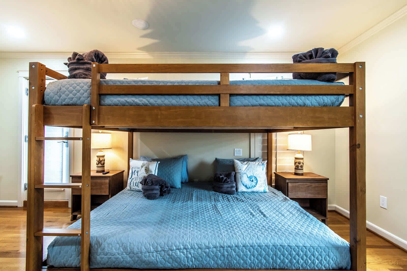 A bunk bed with a blue quilted mattress, wooden headboard, and two bedside tables with lamps.