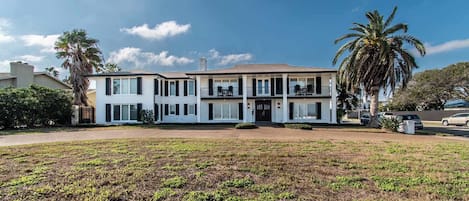 Una casa de dos pisos con un balcón, un césped y una palmera.