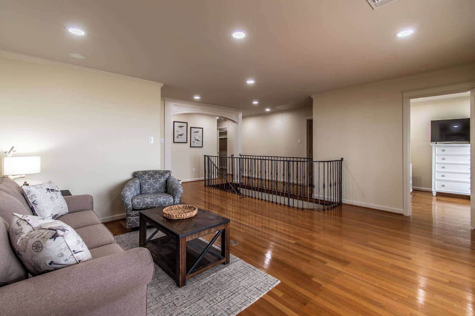 A spacious living room with a sofa, armchair, and coffee table, a staircase leading to an upper level, and a TV in a white cabinet.