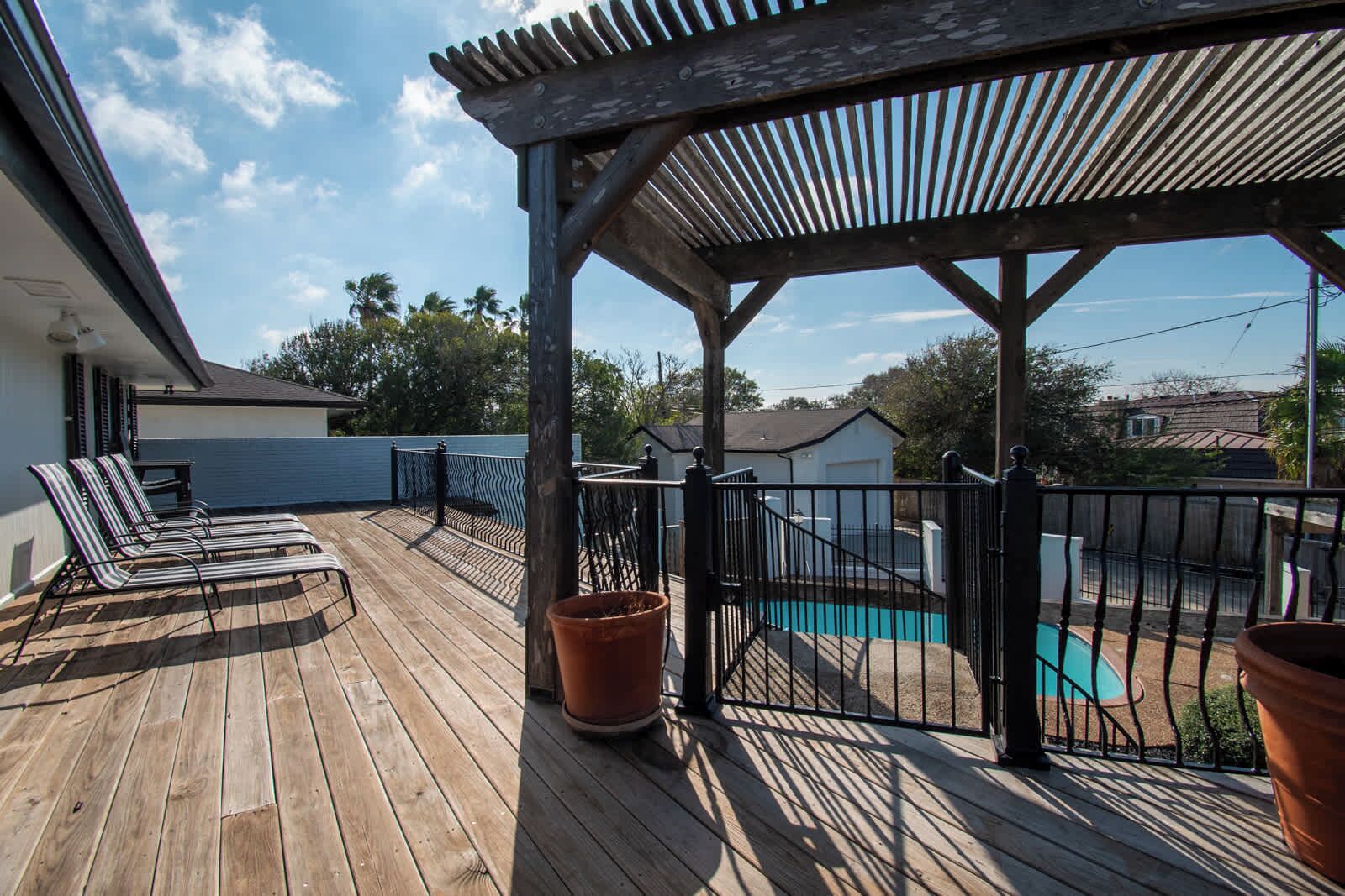 Une terrasse en bois avec des chaises longues, une piscine et un espace abrité doté d’une rambarde.