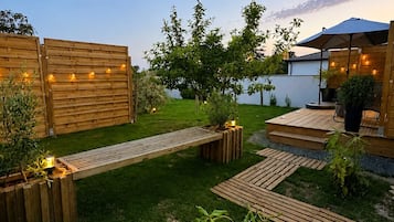 A well-maintained garden with wooden decking, a seating area, and a patio with an umbrella.