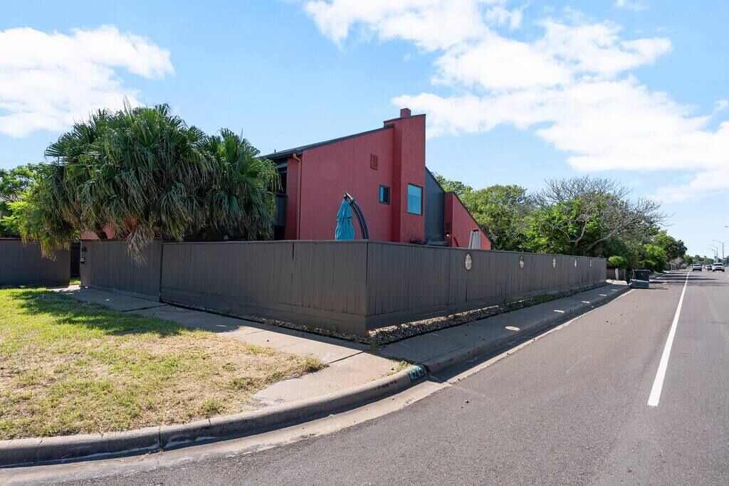 A modern building with a red facade, a gated entrance, and a clear sky.