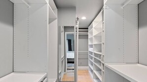 Un petit dressing étroit, avec des étagères ouvertes et un lit en arrière-plan.