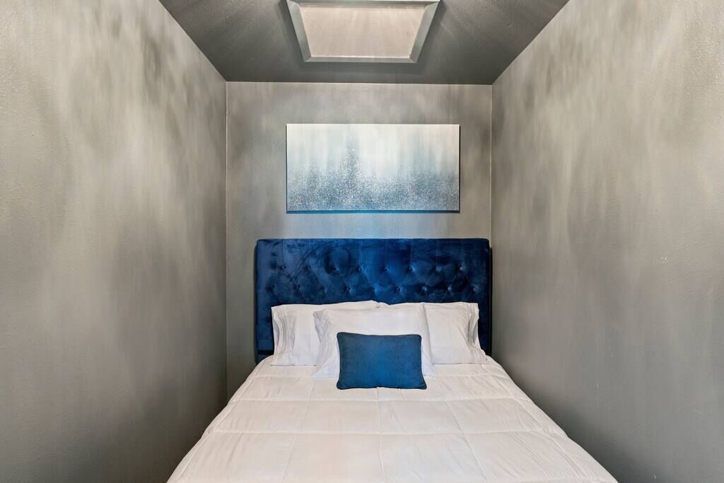 Una habitación de hotel moderna y estrecha con una cama grande, cabecero acolchado y un tragaluz.