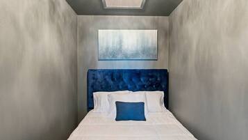 Una habitación de hotel moderna y estrecha con una cama grande, cabecero acolchado y un tragaluz.
