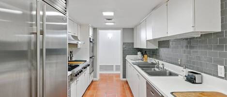 A modern kitchen with stainless steel appliances, white cabinets, and a tiled backsplash.