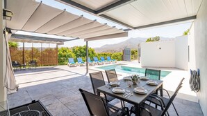 Een buitenterras met zwembad, stoelen en een pergola.