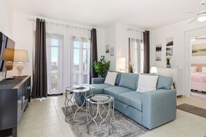 A modern living room with a sofa, two side tables, a TV, and a balcony with curtains. - Beautiful Apartment Callysta PA11 (Kouklia)