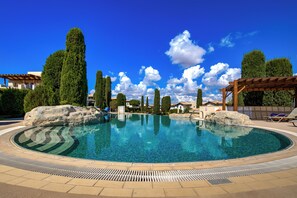 A circular swimming pool with a clear blue center, surrounded by a paved deck, and a pergola structure on the right. - Beautiful Apartment Callysta PA11 (Kouklia)
