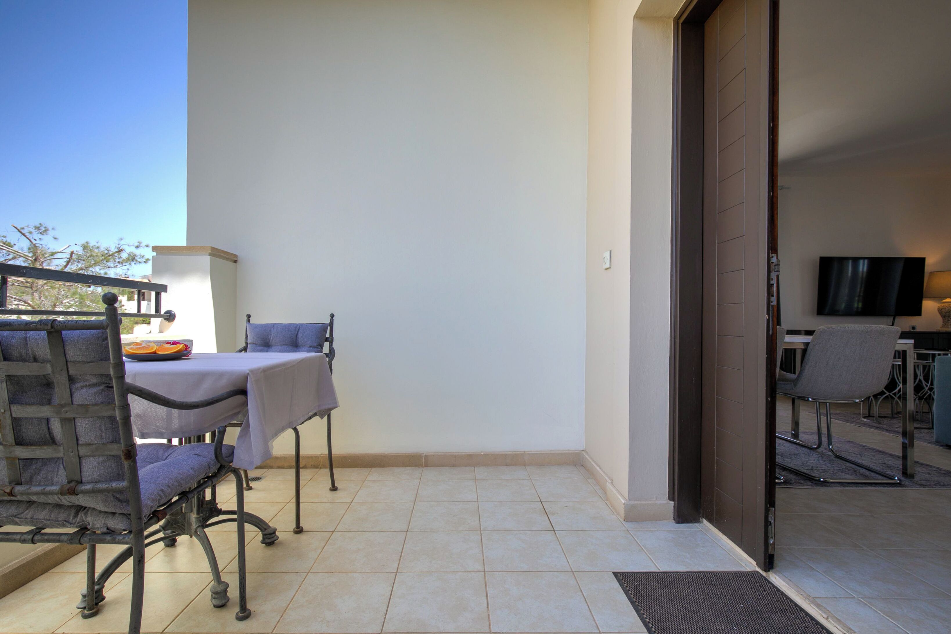 An outdoor patio with a table and chairs, a TV in the background, and a door leading to another room.