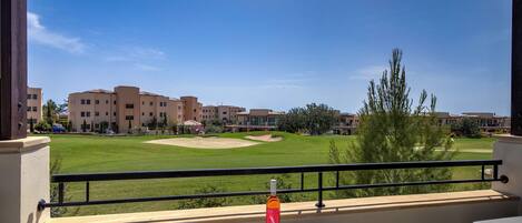 A balcony with a table, a bottle, and a card, overlooking a golf course and buildings.