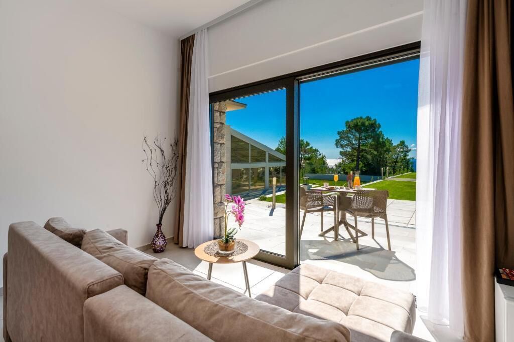 A modern living room with a sofa, a small table with a vase, and a view of an outdoor patio with a table and chairs.
