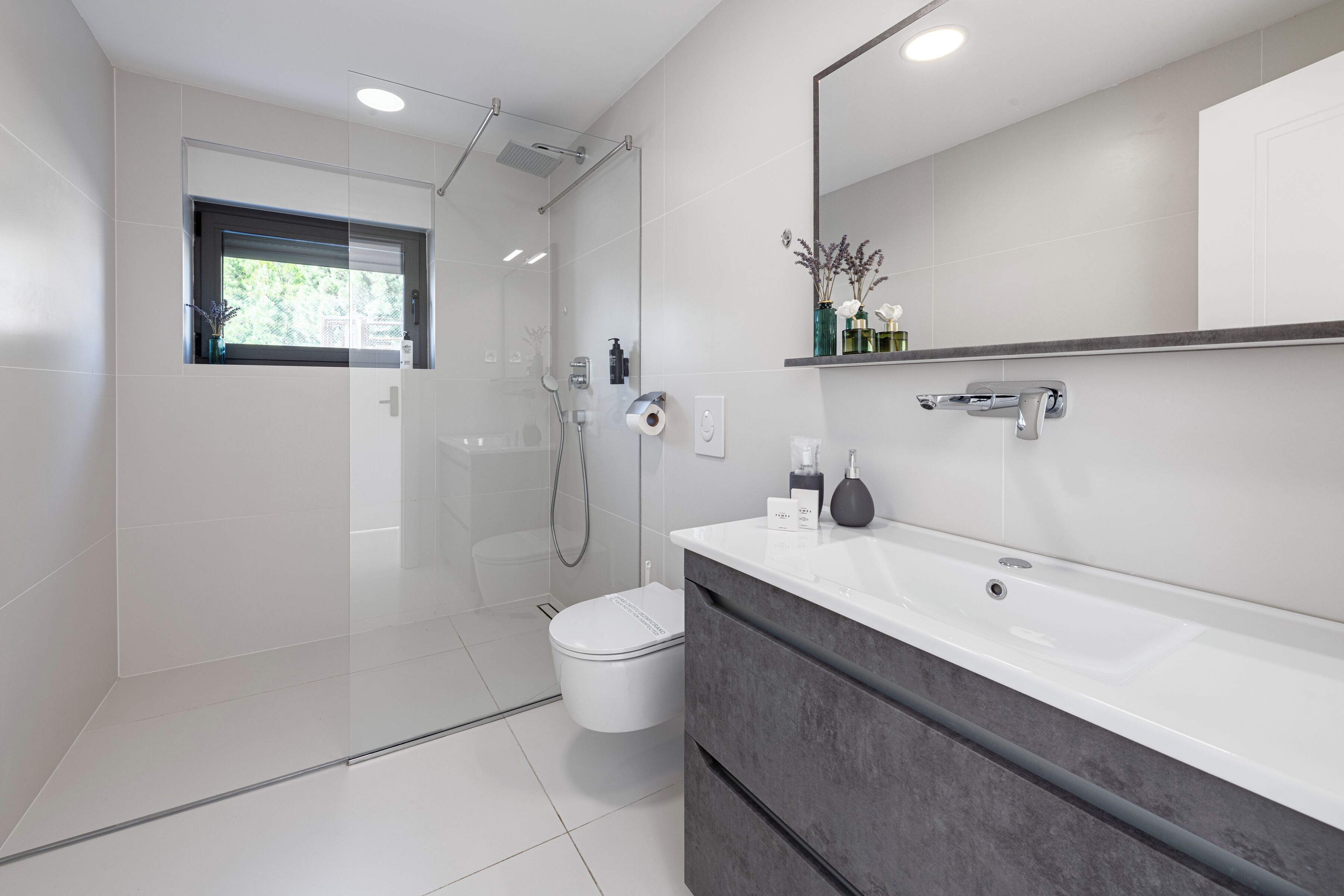 Un bagno moderno con cabina doccia in vetro, un water bianco, un lavabo con specchio e una finestra.