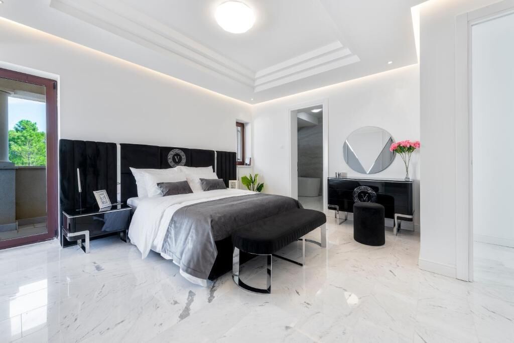 A modern bedroom with a large bed, bedside tables, a bench, and a mirror.