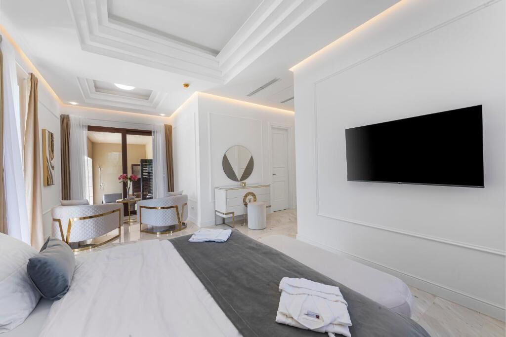 A modern hotel room with a large bed, a flat-screen TV, a vanity with a mirror, and a seating area with chairs.