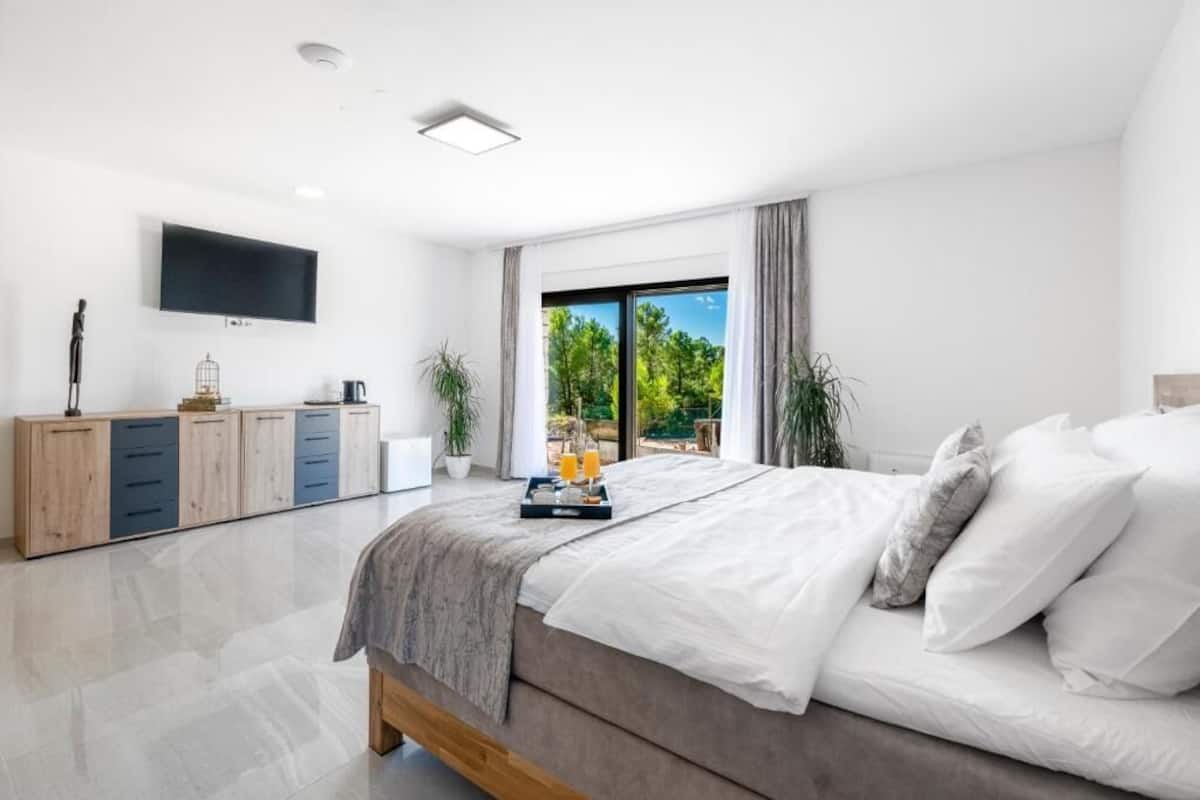 Un dormitorio moderno con una cama grande, un televisor de pantalla plana, un armario de madera y vistas al exterior.