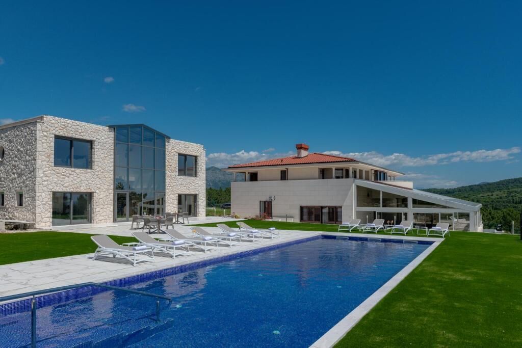Une maison moderne à deux étages, dotée d’une piscine, d’un espace salon extérieur et offrant une vue sur les montagnes.