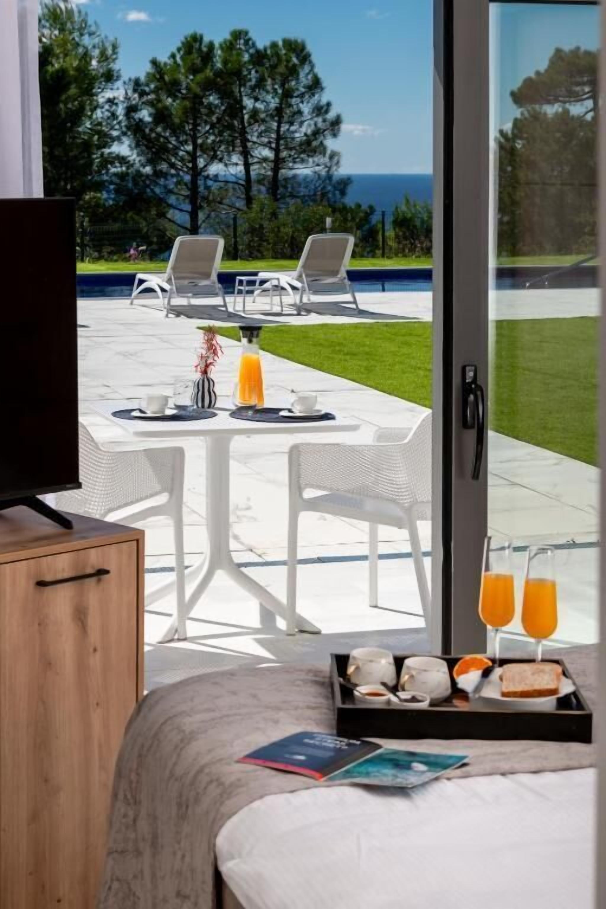 Un dormitorio con cama, televisor, bandeja de desayuno y vistas a una piscina y sillas afuera.
