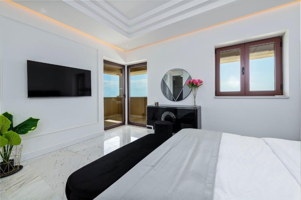 Ein modernes Hotelzimmer mit Flachbildfernseher, einem runden Spiegel, einer Zimmerpflanze und einem Bett mit weißer Bettwäsche.