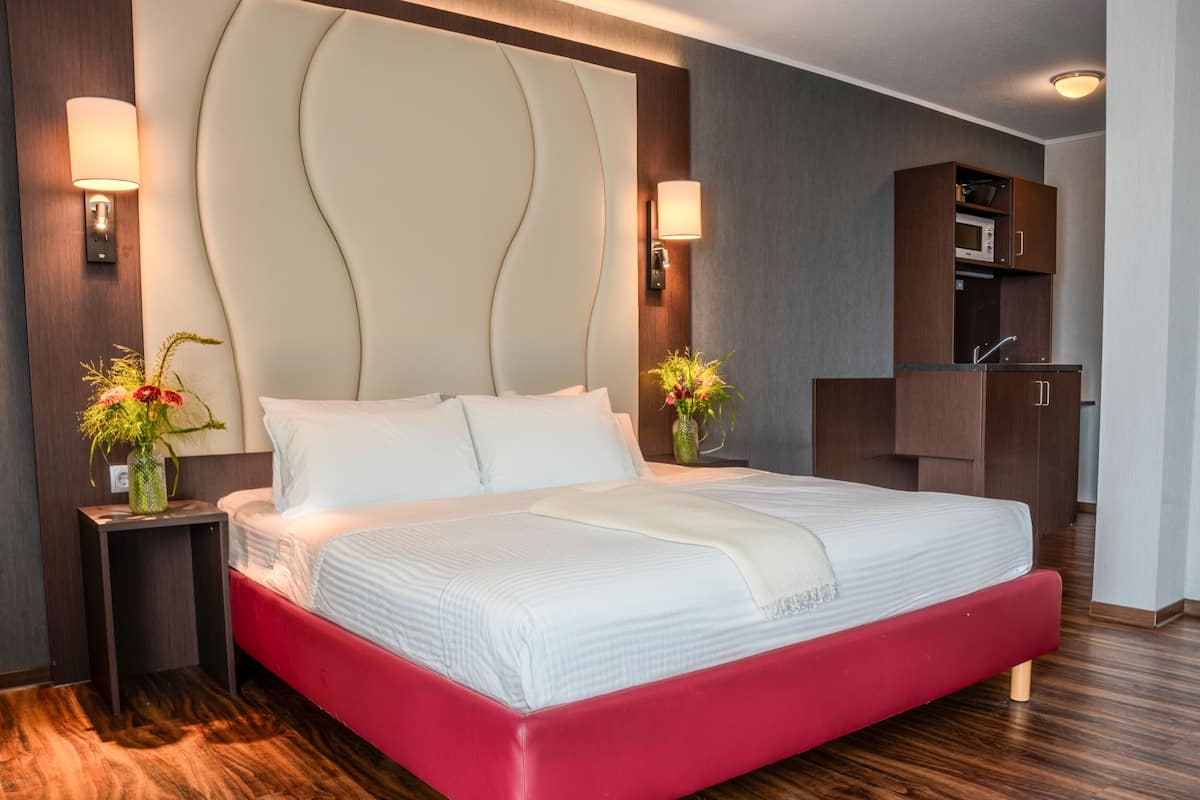 Quarto de hotel moderno com uma cama grande, piso de madeira, guarda-roupa embutido e luminárias de cabeceira.