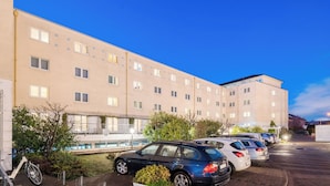 Et hotel med flere etager, parkeringsplads, udendørs pool og grøn bevoksning.