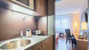 Et lille hotelværelse med tekøkken, seng, skrivebord og stol.