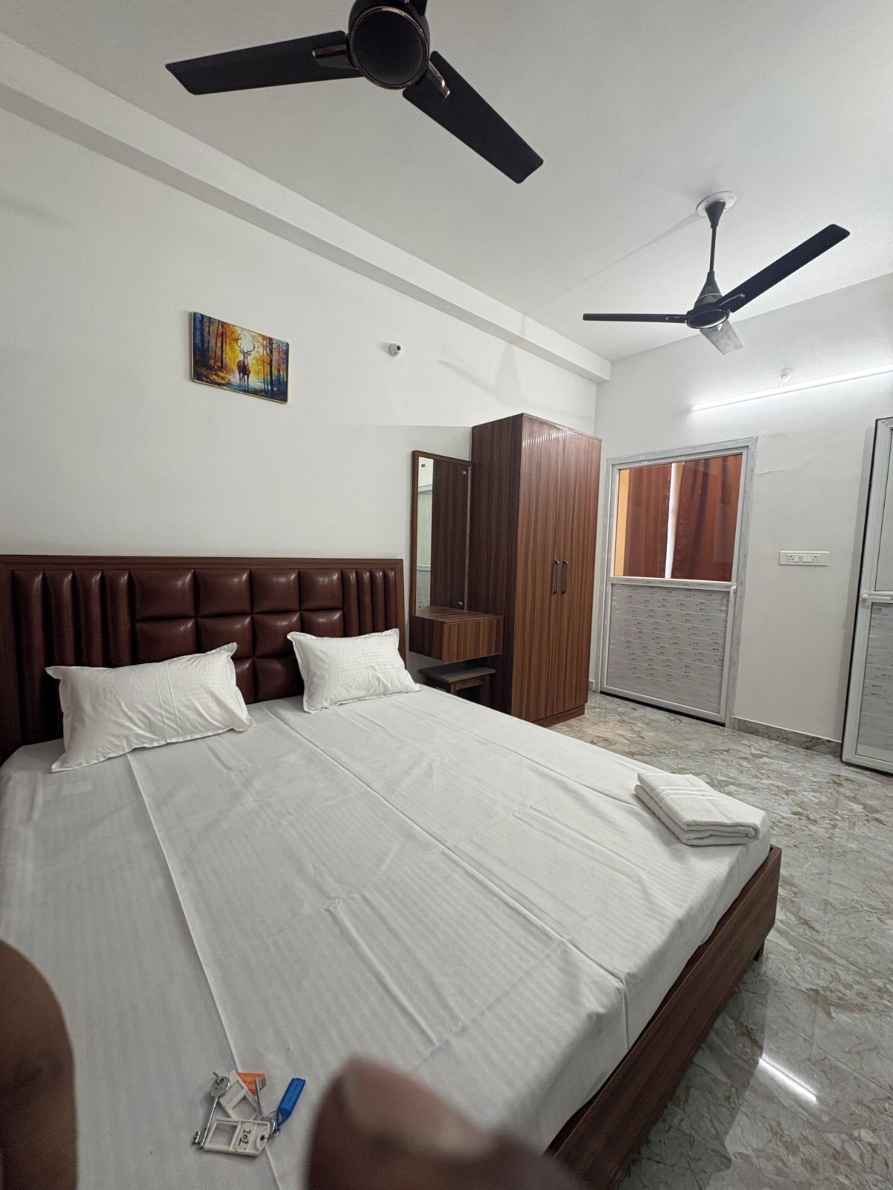 Ein Schlafzimmer mit einem großen Bett, zwei Deckenventilatoren, einem Kleiderschrank, einem Spiegel und einem Fenster mit Jalousien.