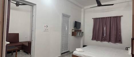 A bedroom with a bed, two ceiling fans, a television on a shelf, a door, and a patterned rug.