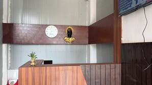 Un mostrador de recepción con un reloj y una estatua de Buda, un televisor montado en la pared y un cubo de basura rojo.