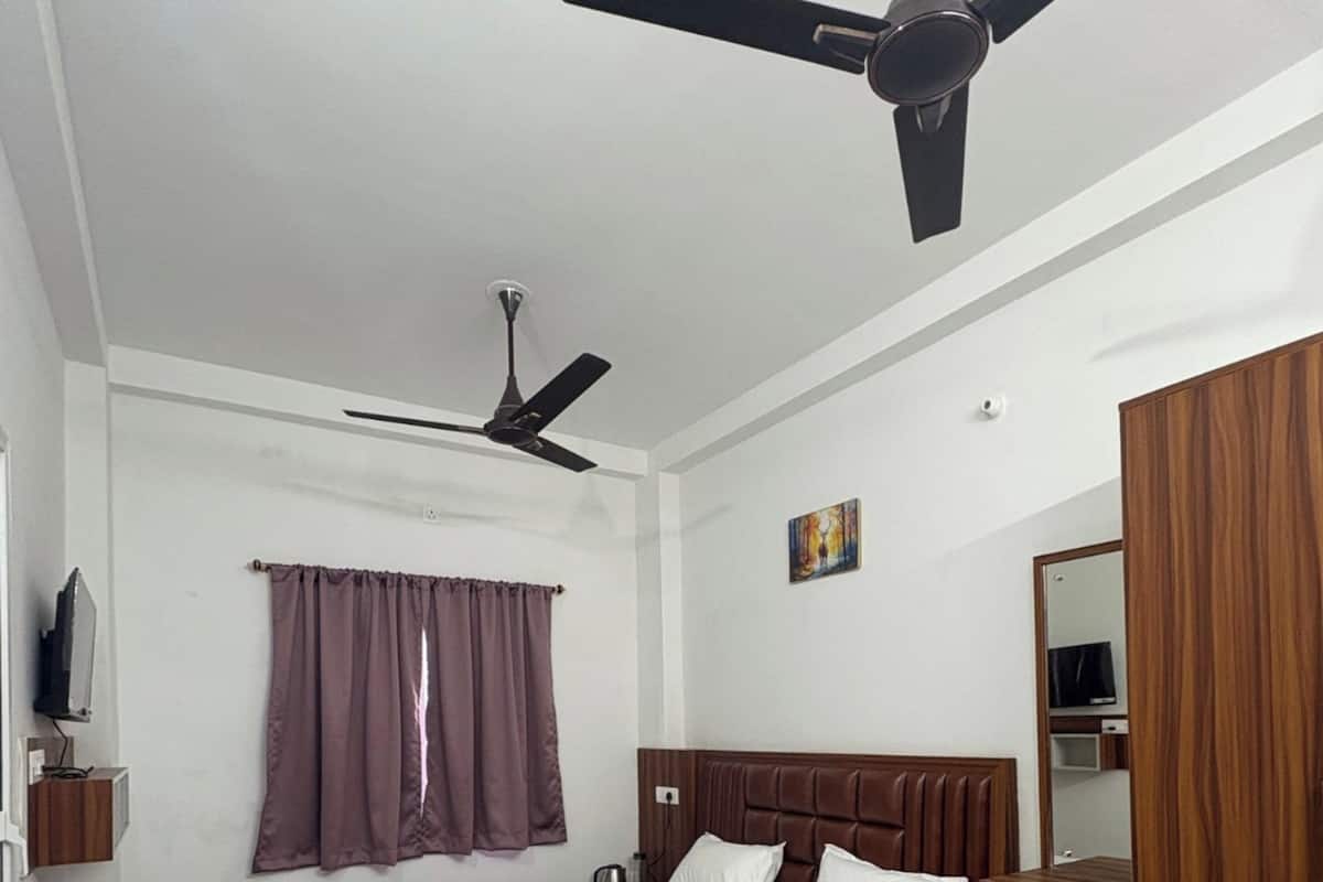 Un dormitorio con cama, ventilador de techo, ventana con cortinas, mesita de noche y armario de madera.