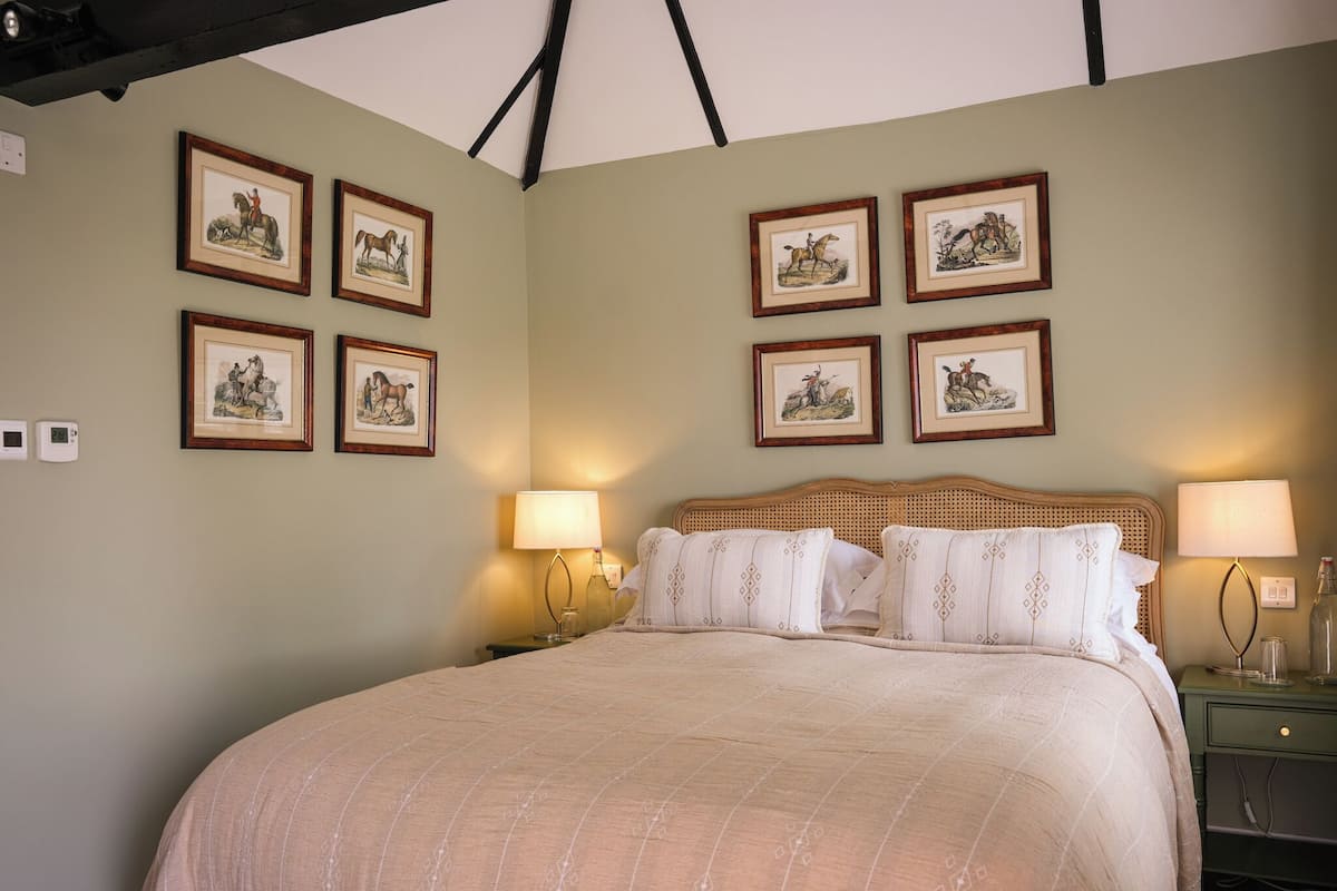 Quarto com uma cama grande, duas mesas de cabeceira com abajures e seis quadros de cavalos na parede.