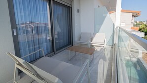 Ein Balkon mit Schiebetür, einem kleinen Tisch, zwei Stühlen und einem Glasgeländer.