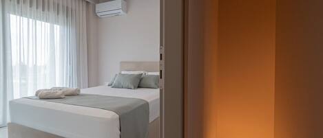 A hotel room with a bed, a bedside table, a window with curtains, and an air conditioning unit.