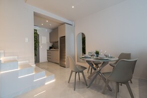 A modern dining area with a round table, four chairs, and a kitchen in the background. - Aria Prive Pool Villa Νο2 by RentalsPro - Portaria Beach (Nea Moudania)