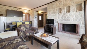 A living room with a fireplace, a television, and a dining area with chairs and a table. - Twin Castles Left Maisonette by RentalsPro (Kassandreia)